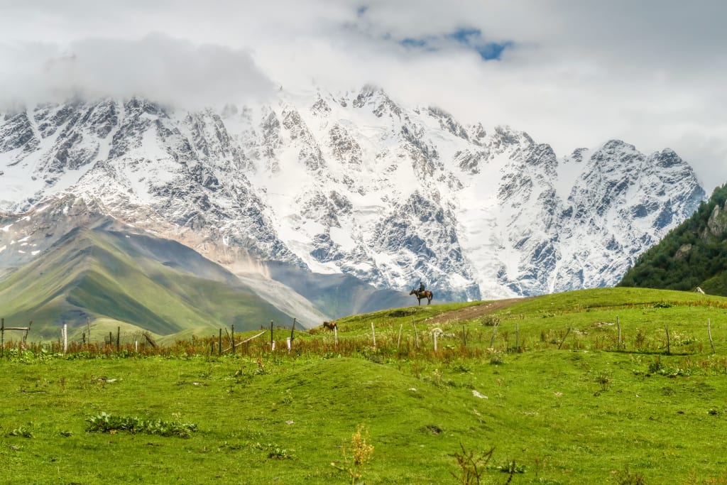 Montagne innevate e campo verde rigoglioso in Georgia nella catena dello Svaneti